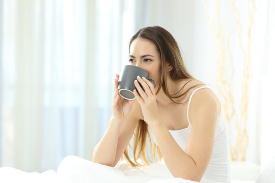 Woman waking up drinking coffee on a bed