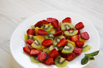 Fresh fruit salad on white wooden background, side view.