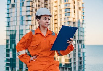 beatiful business woman engineer wearing orange coverall is standing with plan papers. Construction...