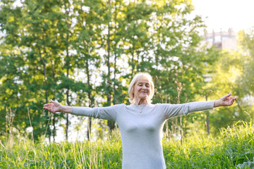 Elderly woman stands with one hand open in a sunny park. How to be happy and active in old age