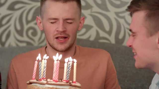 Handsome boy dreamsabout his wish and blows out candles on birthday cake and drinks orange juce