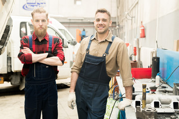 Obraz premium Portrait of young Caucasian male car mechanics in uniform standing in service garage and looking at camera