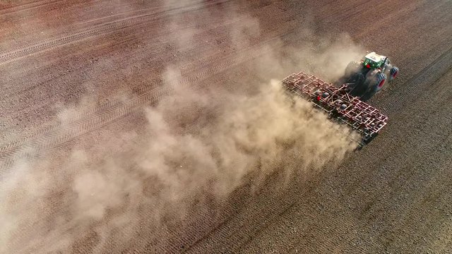 Big Farm Tractor Tilling Dusty Springtime Fields, Aerial View.
