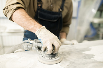 Unrecognizable auto mechanic sanding car detail with grinding machine in repair workshop before painting, close-up view
