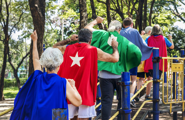 Happy seniors wearing superhero costumes at a playground