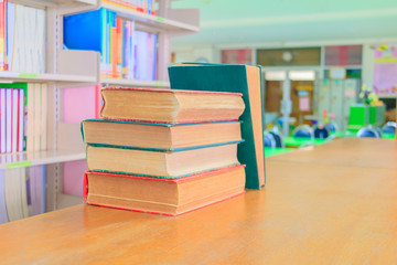 old book red - green. and heap treatise in school library on wooden table.  blurry bookshelves...