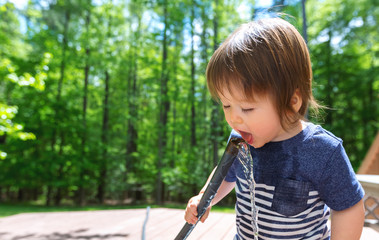 Young toddler boy playing with water from a garden hose outside
