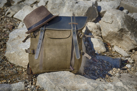 A vintage cloth-leather backpack stands on the stones, on top of the backpack lies a hat. HDR image.