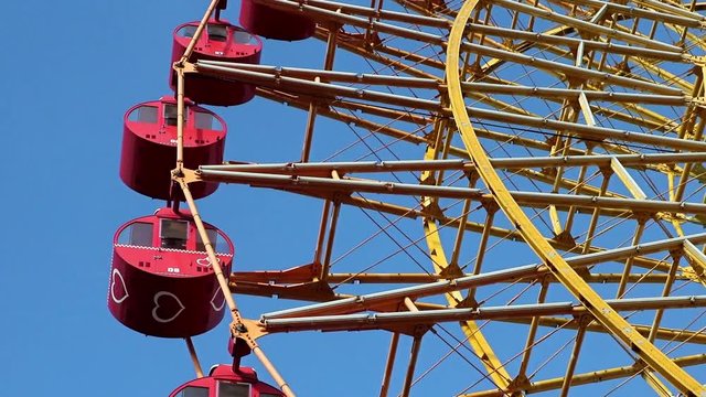 Ferris wheel with red cabins rotate against blue sky.