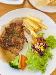 Grilled beefsteak with french fries and vegetables on white dish.