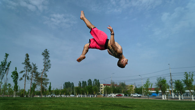 Tricking on lawn in park. Man does somersault back to sky background. Martial arts and parkour. Street workout.