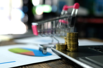 Step of coins stacks with trolley and notebook laptop computer and financial graph on paper on working table, business planning vision and finance analysis concept.