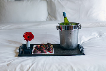 tray with champagne and strawberries on bed 