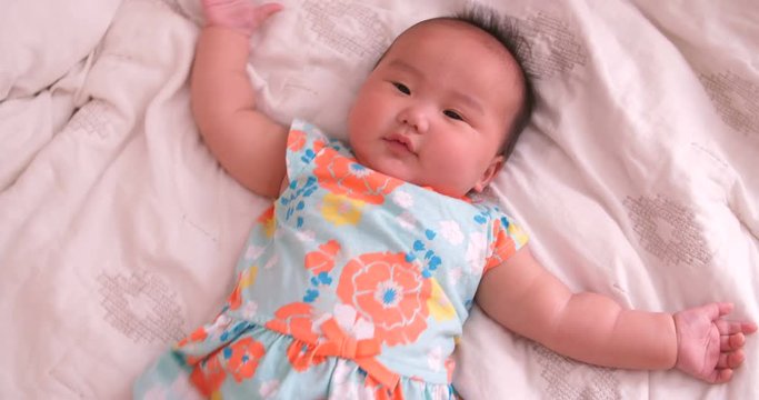 Asian baby girl laying on the bed kicking and laughing into the camera while playing