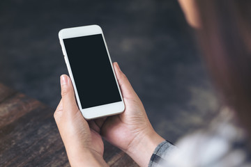 Mockup image of woman's hands holding white mobile phone with blank black desktop screen in cafe