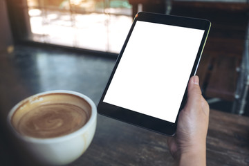 Mock up image of hands holding black tablet pc with white blank screen while drinking coffee in cafe