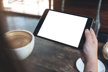 Mock up image of hands holding black tablet pc with white blank screen while drinking coffee in cafe