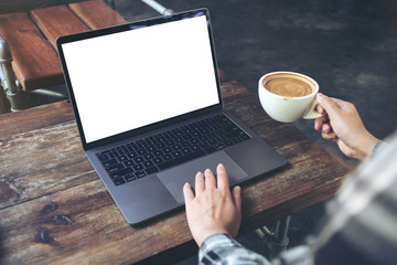 Fototapeta premium Mockup image of a woman using laptop with blank white desktop screen while drinking hot coffee in cafe
