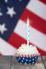 Patriotic 4th of July celebration cupcake with a candle. The American flag in the background. 