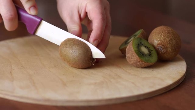 Close-up of a woman cuts a ripe kiwi with a ceramic knife on a round cutting Board at home in the kitchen. Diet. The concept of healthy eating and lifestyle.
