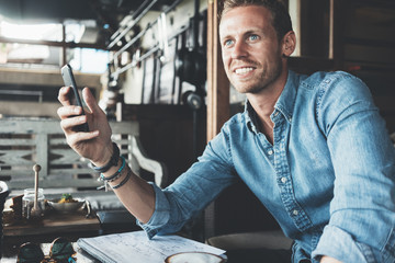 Cheerful entrepreneur working on business project in city cafe with mobile phone and paper