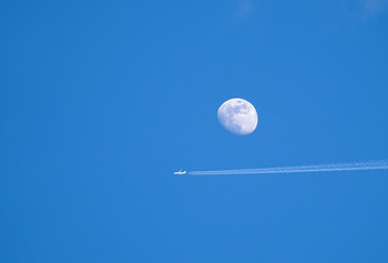 airplane with contrail on sky and moon