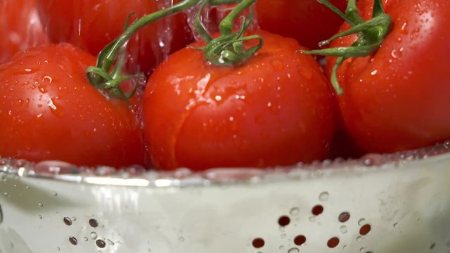 Dolly: Closeup of fresh tomatoes in steel colander under running water in slow motion.