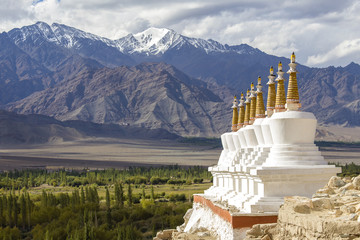 Buddhist chortens, white stupa and Himalayas mountains in the background near Shey Palace in...