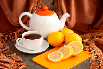 Tea with lemon on the background of velvet curtains. A tea cup, teapot, sliced and whole lemons on the background of luxurious velvet curtains. Tea with lemon is a classic.