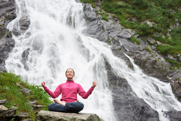 Young woman meditating relaxing alone against waterfall Balea in Fagarash mountains. Rocky...