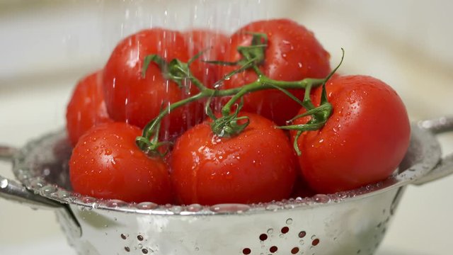 Washing fresh tomatoes in steel colander under running water before cooking and eating