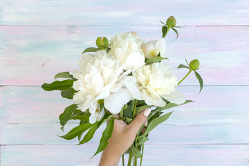A bouquet of pions in the hands of a girl. Peonies on a wooden background. Texture. A photo for social networks. Flat lay desks