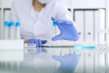 Close-up of professional female scientist in protective eyeglasses making experiment with reagents in laboratory. Medicine and research concept