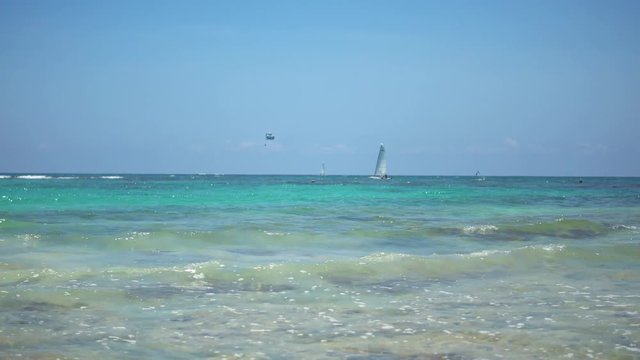 View of tropical beach. Tourists ride parasailing boat with parachute. Sailing yacht sails on waves. Turquoise water of the Caribbean Sea. Riviera Maya Mexico.