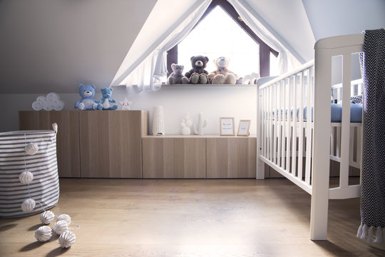 Modern scandinavian nursery interior with toys, teddy bears, baby cot and cotton bowls lamps. Sunny and bright room.