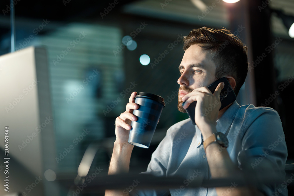 Wall mural young fatigue man speaking on phone and holding paper cup while watching computer in office working 