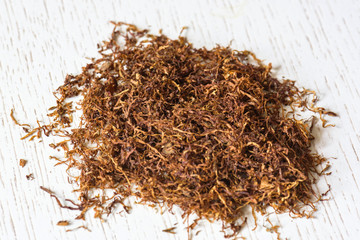 A pile of natural cigarette tobacco on a white wooden table. Nicotine addiction. Health hazard.