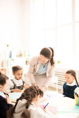 Fototapeta premium Teacher teaching kids in classroom at school. They are sitting together at the table and drawing
