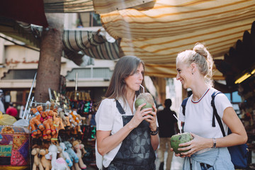 Two young happy women with coconuts at traditional bazaar in Dubai, UAE