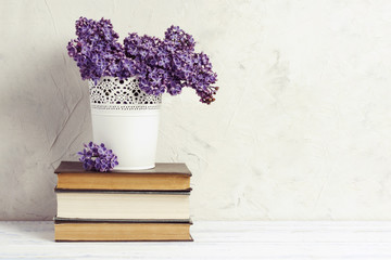 Lilac in a white decorative bucket on a pile of books on a white stone background