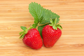 Two garden strawberries with leaf on wooden surface
