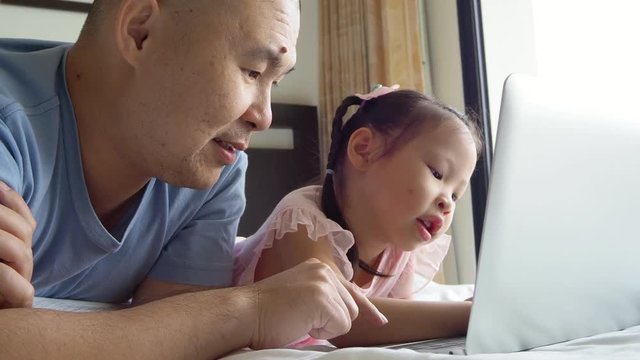 Asian father and daughter using laptop computer on bed
