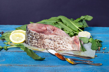 raw fish steak on paper with greens, lemon and spices on a blue 