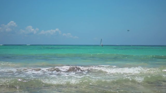 View of tropical beach. Tourists ride parasailing boat with parachute. Sailing yacht sails on waves. Turquoise water of the Caribbean Sea. Riviera Maya Mexico.
