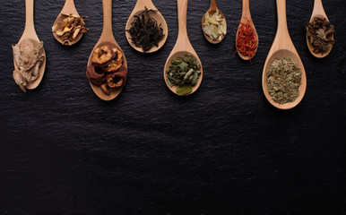 Fototapeta na wymiar Various kind of dried leaves, fruit and flower put in many kind of wooden spoons on black background with copy space.