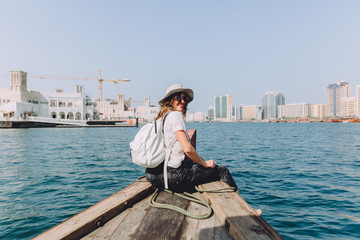 Young beautiful woman sitting at boat and looking at sea and the city DUbai