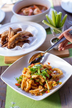 Deep fried battered hot and spicy calamari cook with black pepper and bell pepper with a hand holding a spoon.