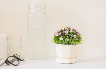 Plastic flower bouquet  in a pot placed on a white wooden in a bed room