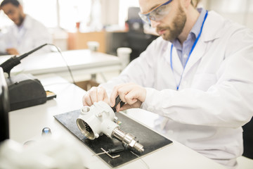 Serious busy male engineer in lab coat assembling modern manometer using pliers while working in...