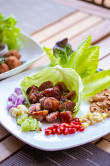 A dish of Thai style fermented sausage with side herbs, chili, lime, ginger, cashew nut. garlic and shallot on dining table.